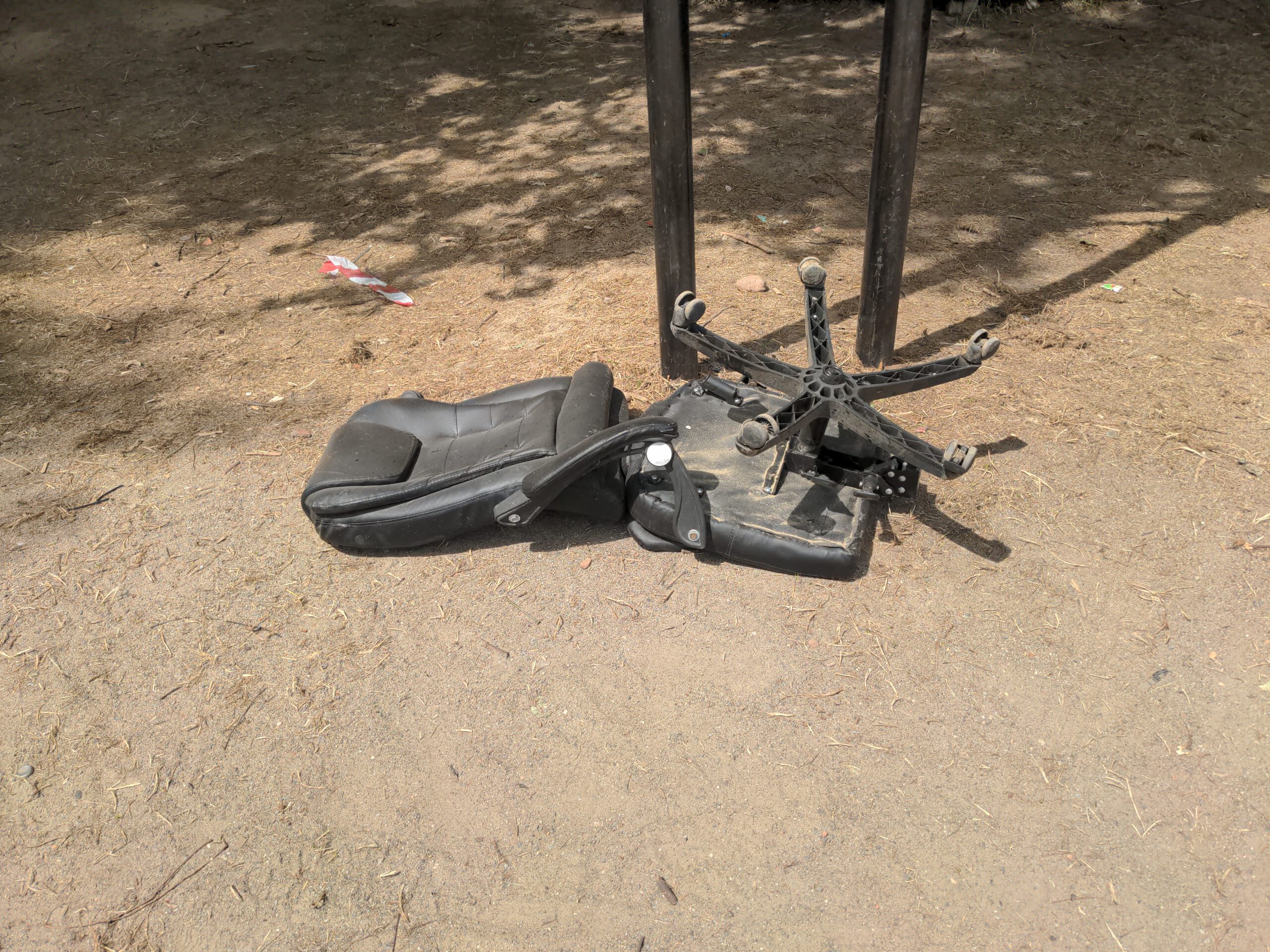 Foto of a broken office chair laying in the sand. The way the chair is broken gives a feeling of a humanized object, the chair looks like it was falling while moving forward.